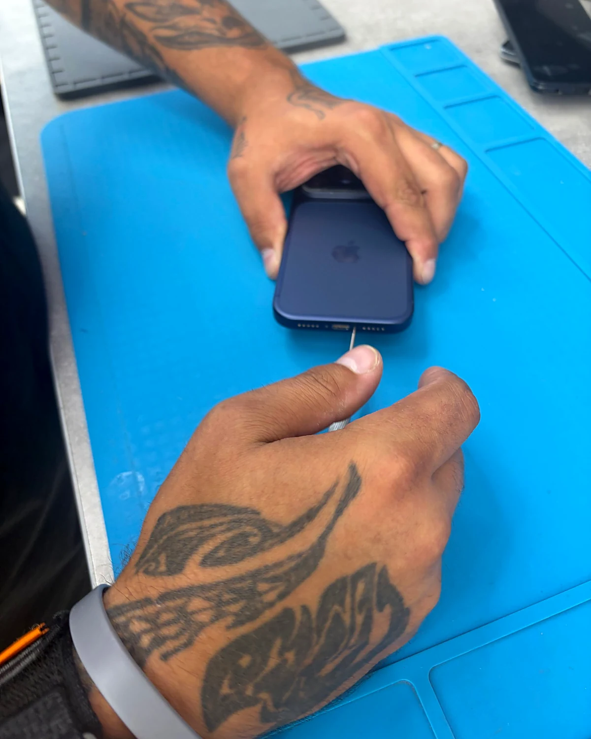 Greg, réparateur chez Phone Games, ouvre un iPhone sur un tapis de réparation bleu
